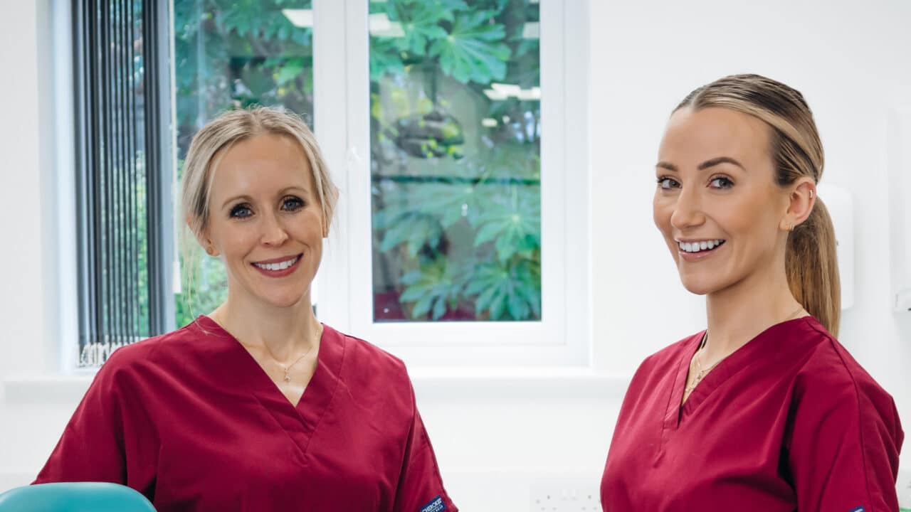 Dr Hannah Wilson and another female clinician smiling into the camera wearing maroon scrubs