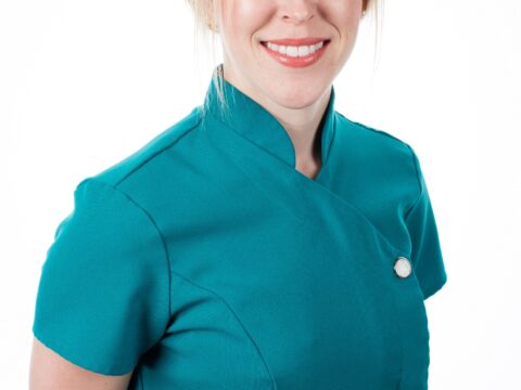 Dr Hannah Wilson, a blonde woman smiling into the camera wearing a teal tunic with her hands behind her back